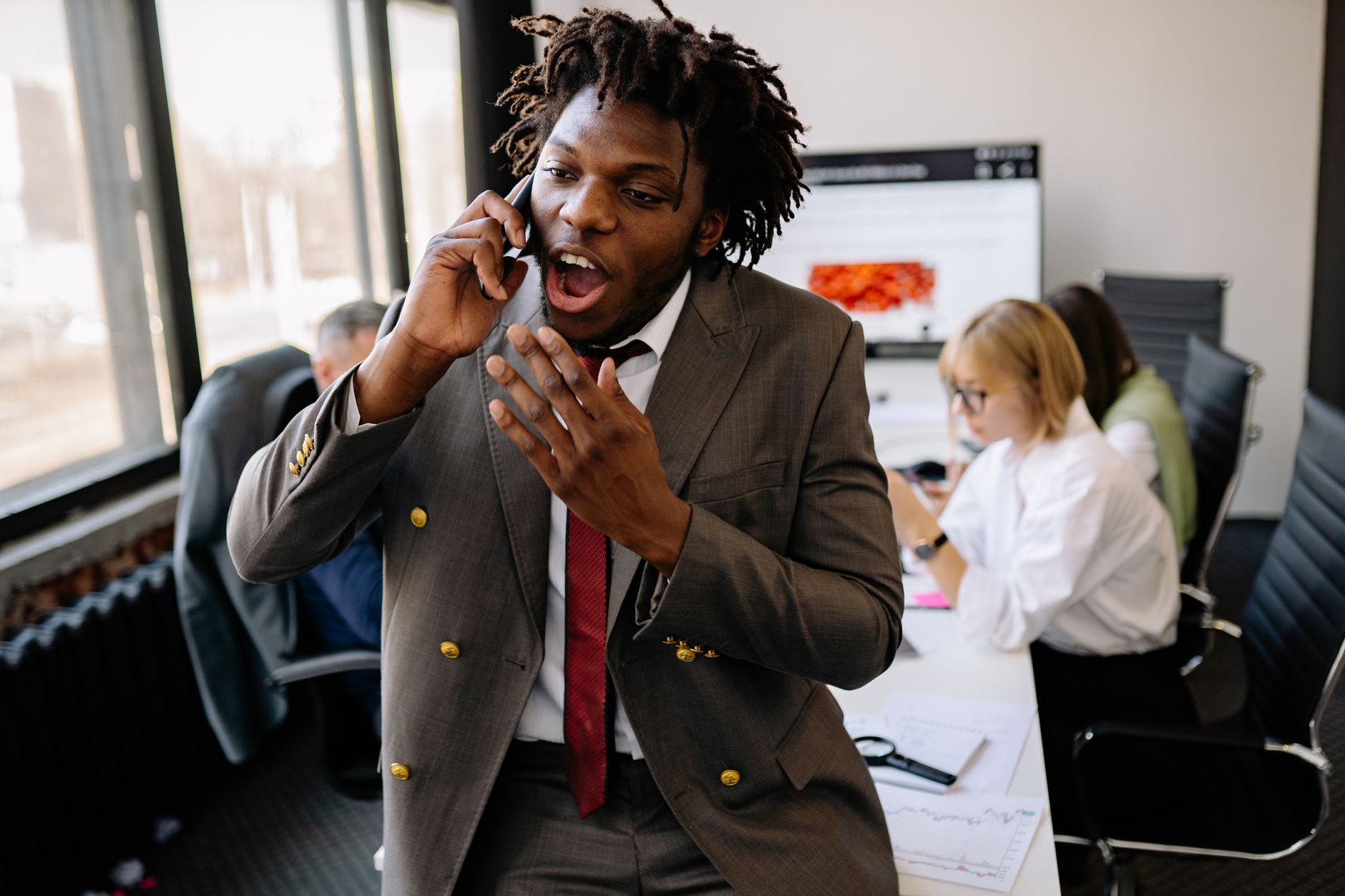 Energetic businessman in a suit having a phone call in a busy office environment.